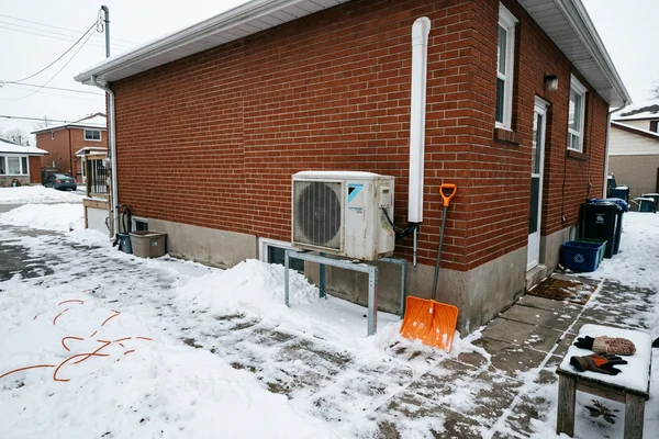 Cold-climate heat pump outdoor unit on a raised snow stand beside a detached GTA home