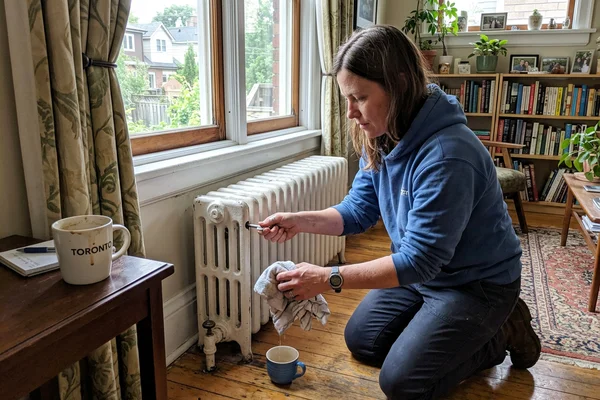 Technician bleeding air from a cast iron radiator in an older Toronto semi-detached house