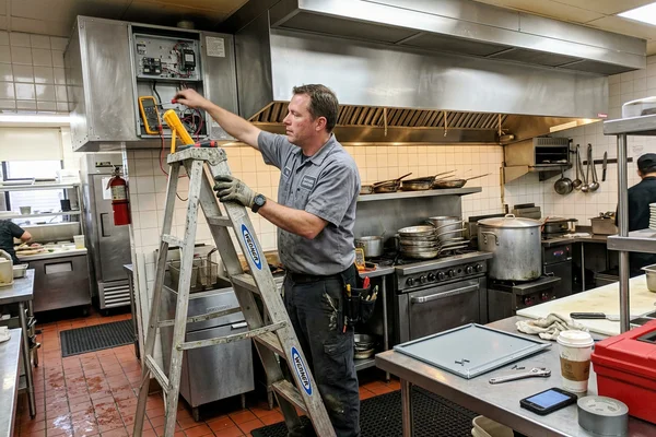 Technician servicing a make-up air unit beside the exhaust hood in a Toronto restaurant kitchen
